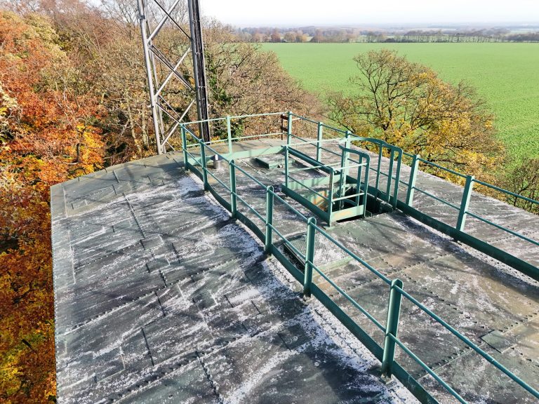 Aerial view of a remote water tank with railings atop a tower, surrounded by autumn foliage.