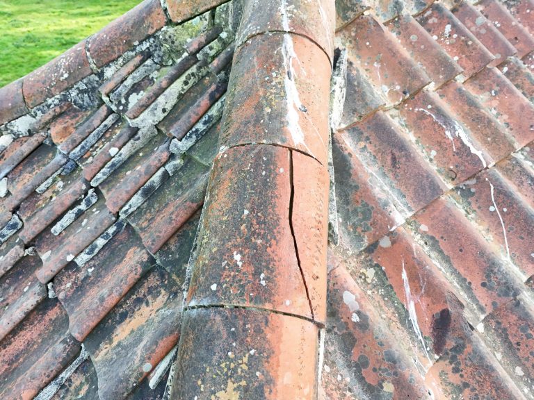 Weathered terracotta roof tiles with moss, cracked tile and uneven surfaces.