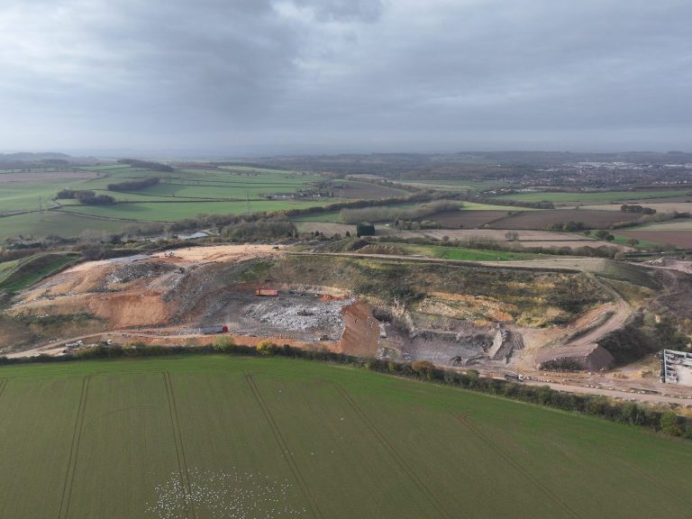 Aerial view of a landfill site surrounded by fields and rolling hills under a cloudy sky.