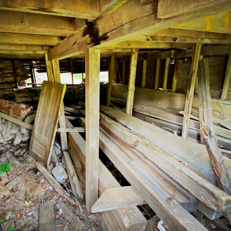 Interior of a dilapidated barn with scattered wooden planks and debris.