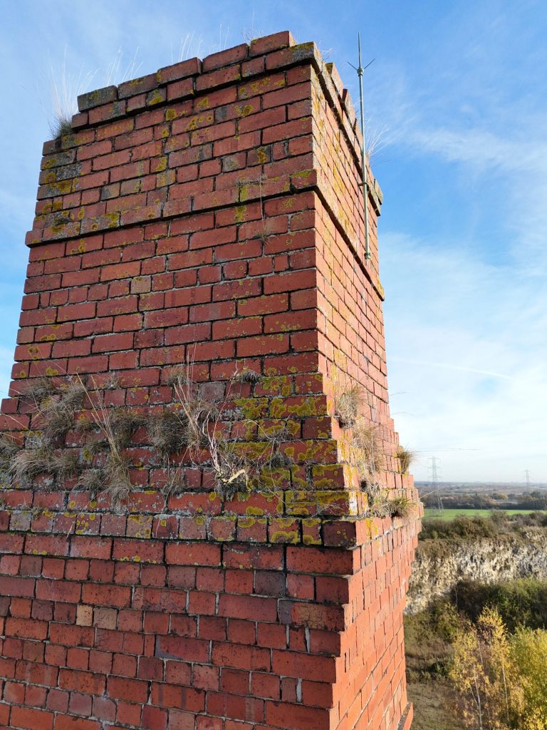 Brick chimney with moss, featuring a partly weathered structure against a clear sky.