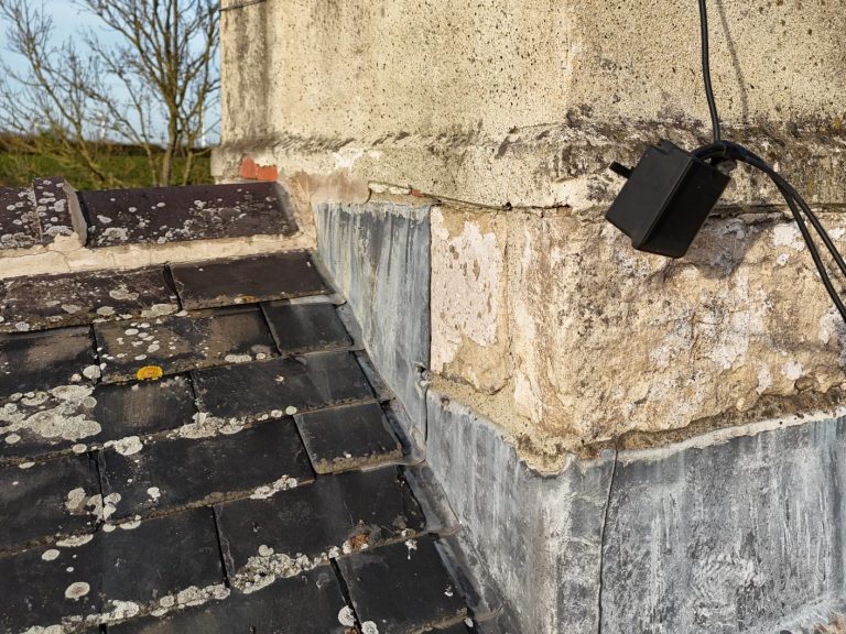 Close-up of a weathered stone chimney with a loose aerial junction box.