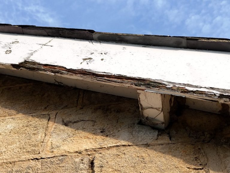 Close-up of a weathered roof edge showing cracks and peeling paint against a blue sky.