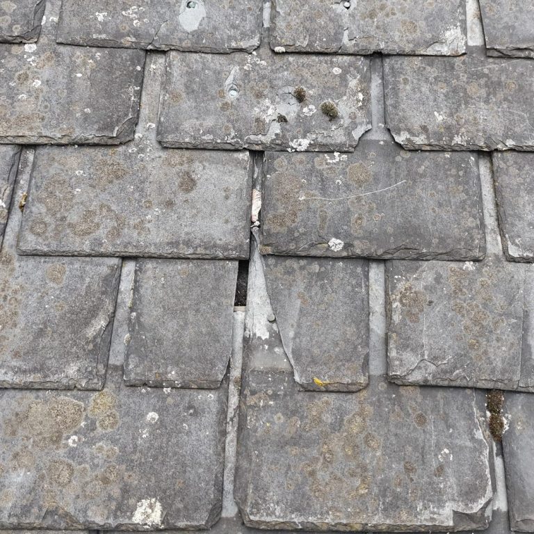 A slate house roof with a broken tile exposing a hole.