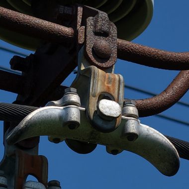 Close-up of metal components and wires on an electricity pylon against a blue sky.