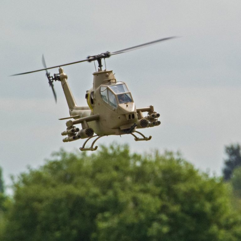 Radio controlled model military helicopter hovering over greenery.