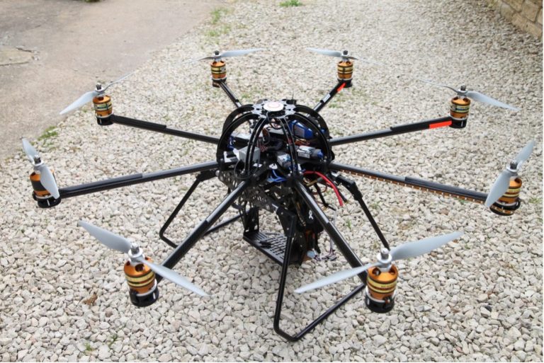 A large octocopter drone with multiple rotors and a complex frame, placed on gravel.