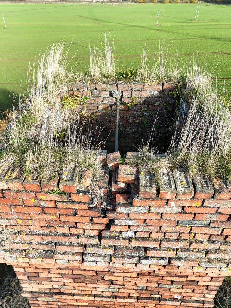 Overgrown brick structure with grass and weeds growing from the top.