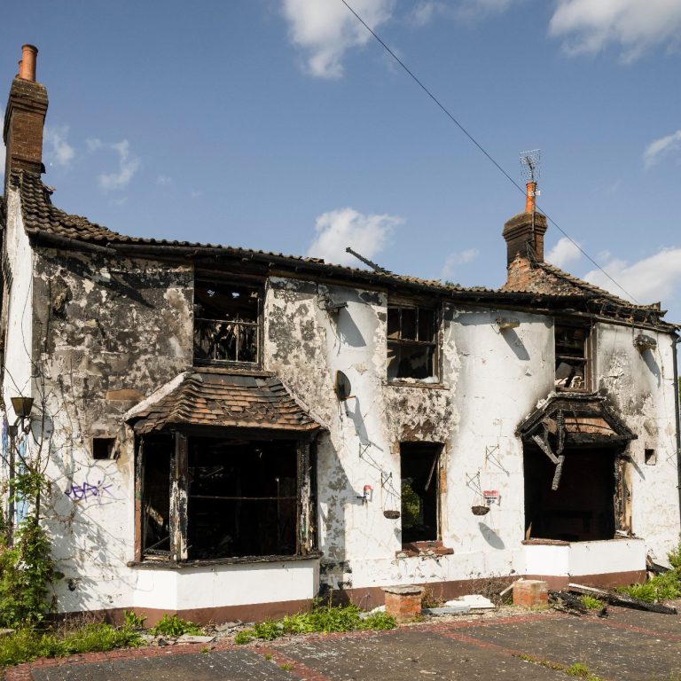 Abandoned, burn-damaged house with charred walls and broken windows.