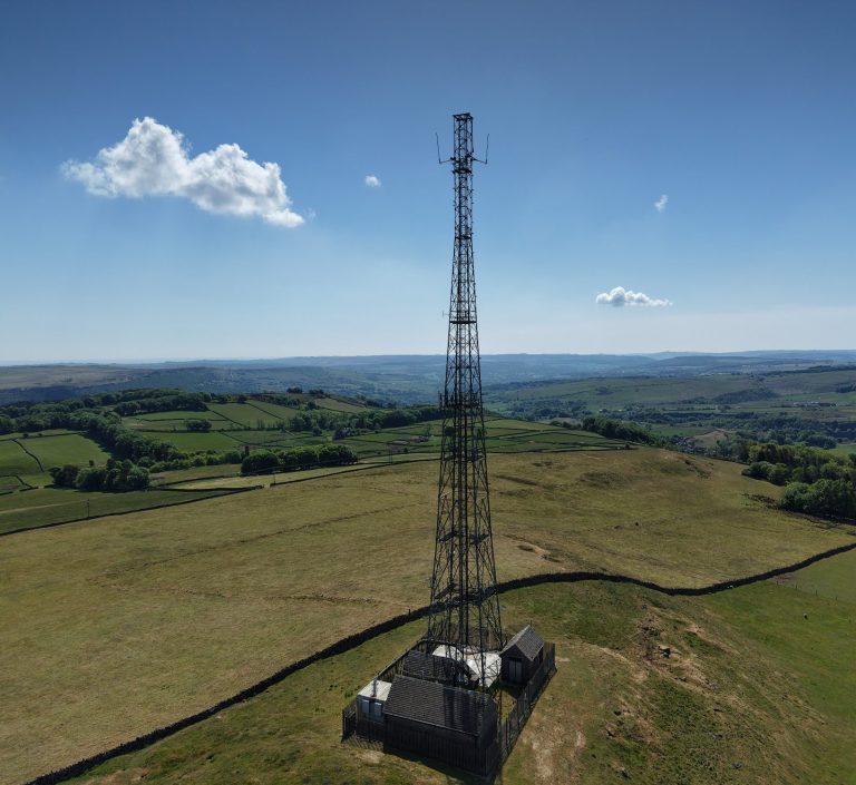 Communications tower on a hilltop with a clear sky and surrounding green landscape.