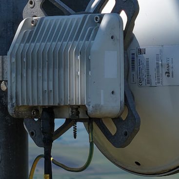 Close-up of a microwave dish mounted on a telecoms mast with cables attached.