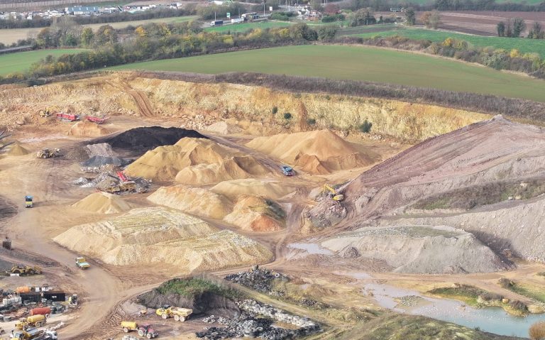 Aerial view of a construction site with piles of sand and gravel in a rural landscape.