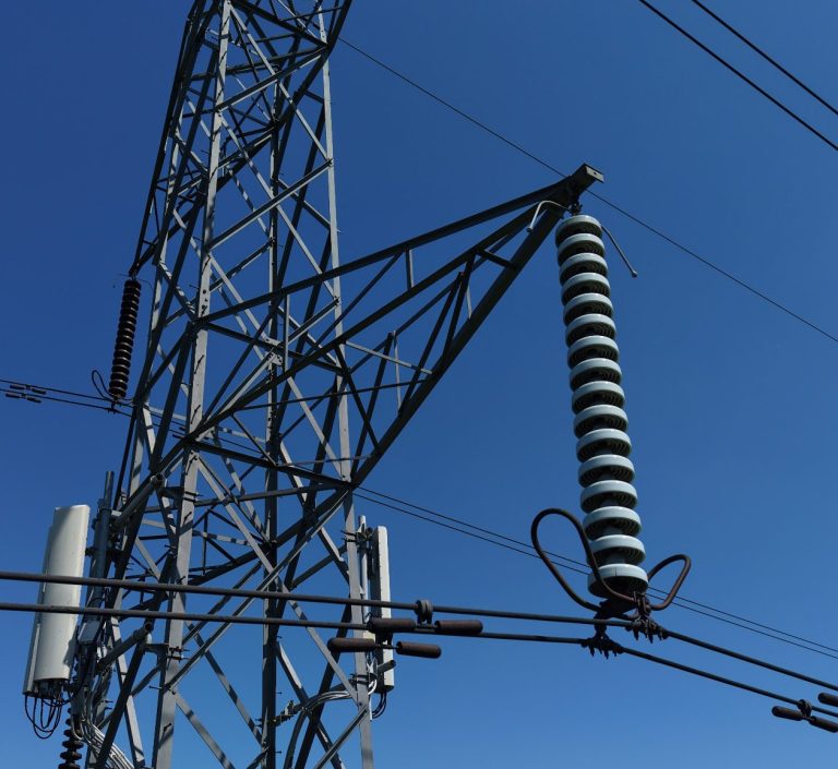 Electricity pylon against a clear blue sky, featuring insulators and cables.