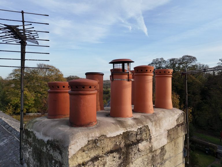 A row of red brick chimney stacks atop a stone wall against a clear sky.