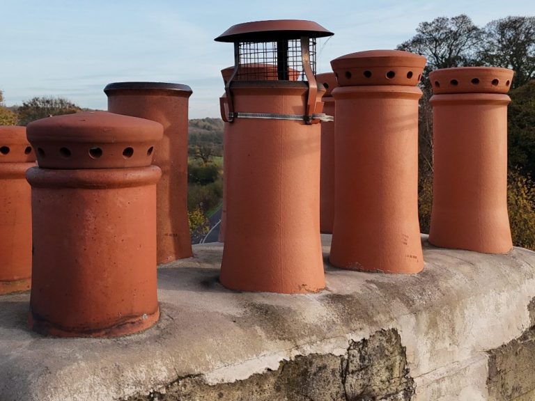Row of terracotta chimney pots with varied designs on a rooftop.