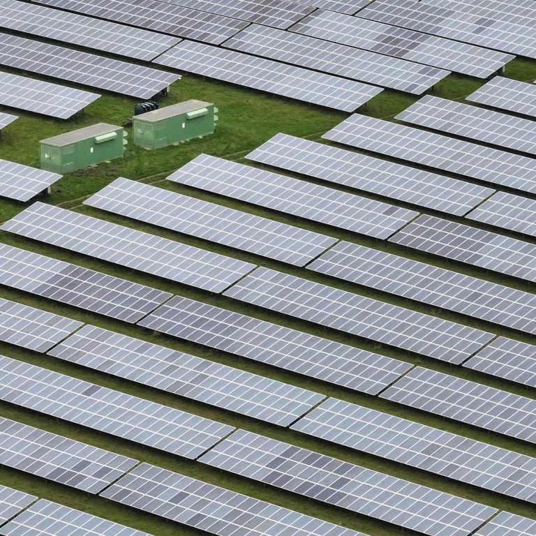 Expansive solar panel array with two green storage units on grassy land.