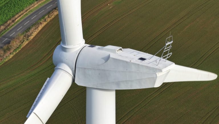Close-up of a wind turbine rotor and nacelle against a green landscape.